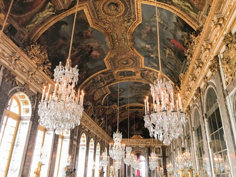 The ceiling art and crystal chandeliers in the Hall of Mirrors at the Palace of Versailles outside of Paris, France.