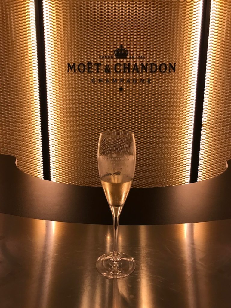 A glass of champagne sitting in front of a Moet et Chandon Champagne sign in Epernay, France.