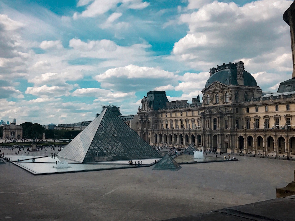 An image from inside the Louvre Museum with part of the Lourve and the pyramids in front of the Lourve in Paris, France.