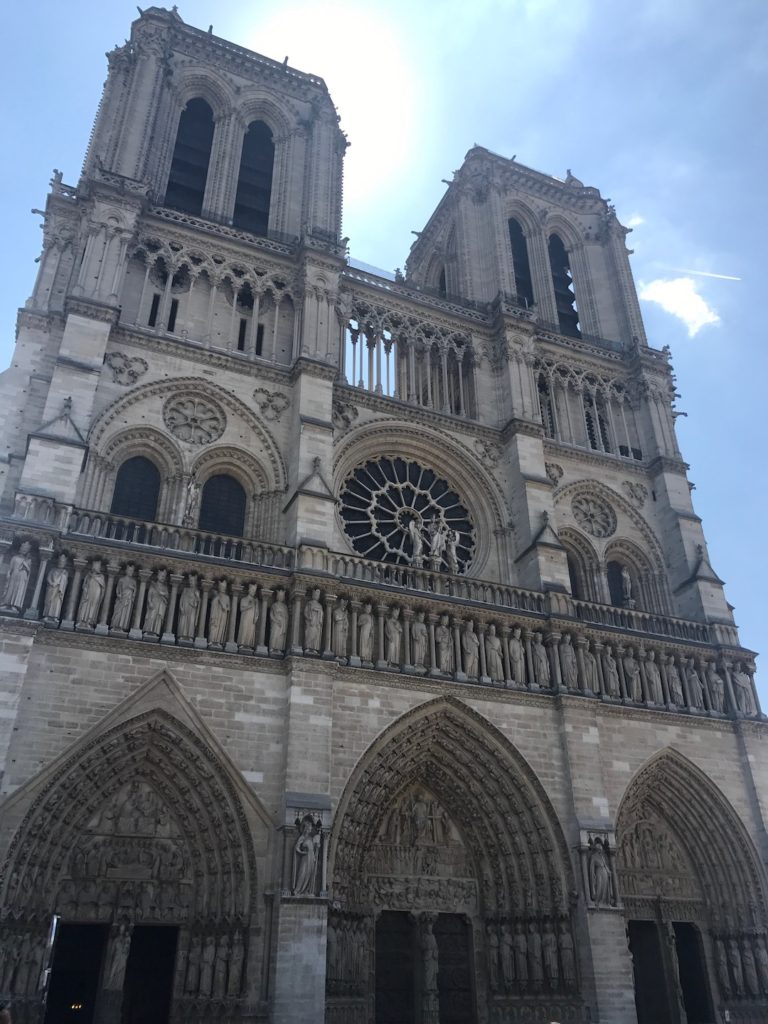 Image of the front side of the Notre Dame with the sun shining behind it in Paris, France.
