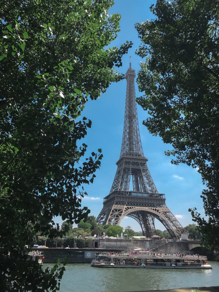 An image of the Eiffel Tower from the other side of River Seine looking through the trees.