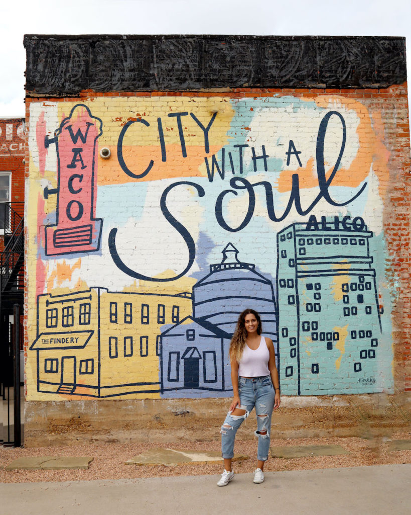 Me, Say Sarah, standing in front of a mural in Waco, Texas stating "Waco - a city with a soul"