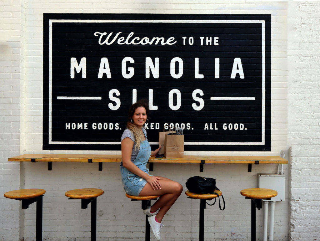 Me, Say Sarah, siting in front of the "Welcome to the Magnolia Silos" sign at the Magnolia Market in Waco, Texas by Chip and Joanna Gaines.